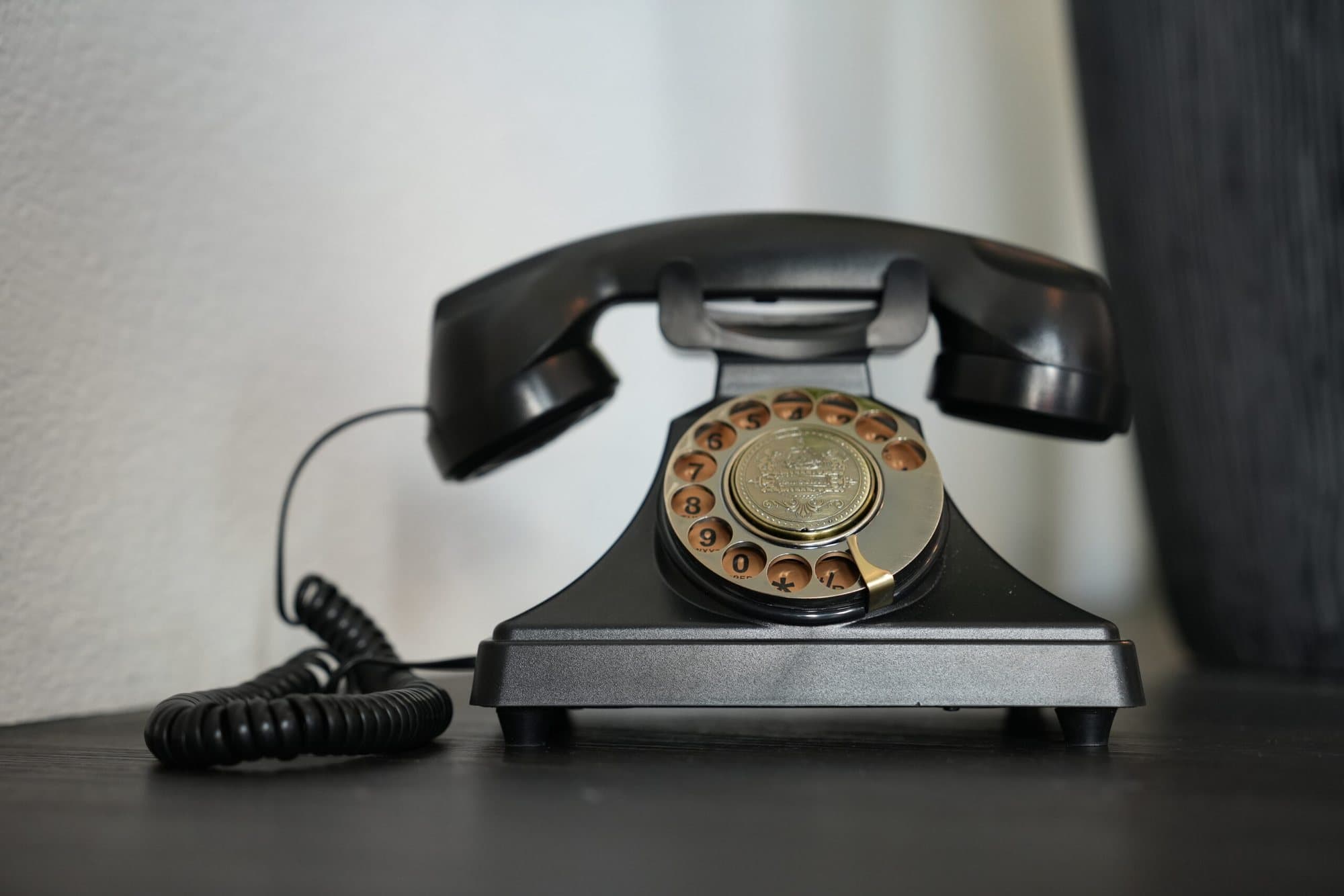 Schwarzes Retro-Telefon mit goldener Wählscheibe als Audio-Gästebuch auf dunklem Holztisch