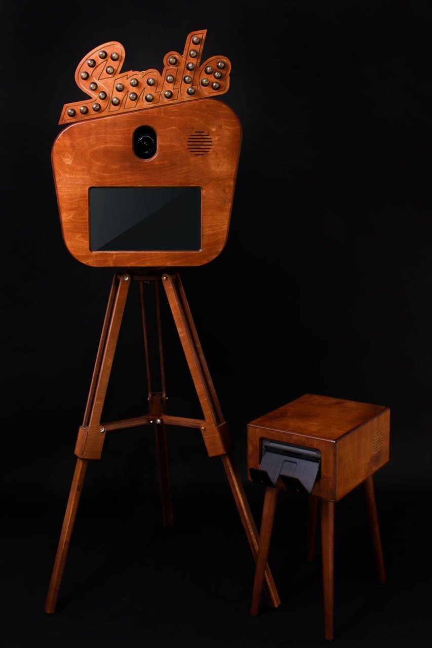 Fotobox «Smile» auf Holzstativ, daneben der Fotodrucker im Holzkasten mit Ausgabeschlitz für Fotostreifen