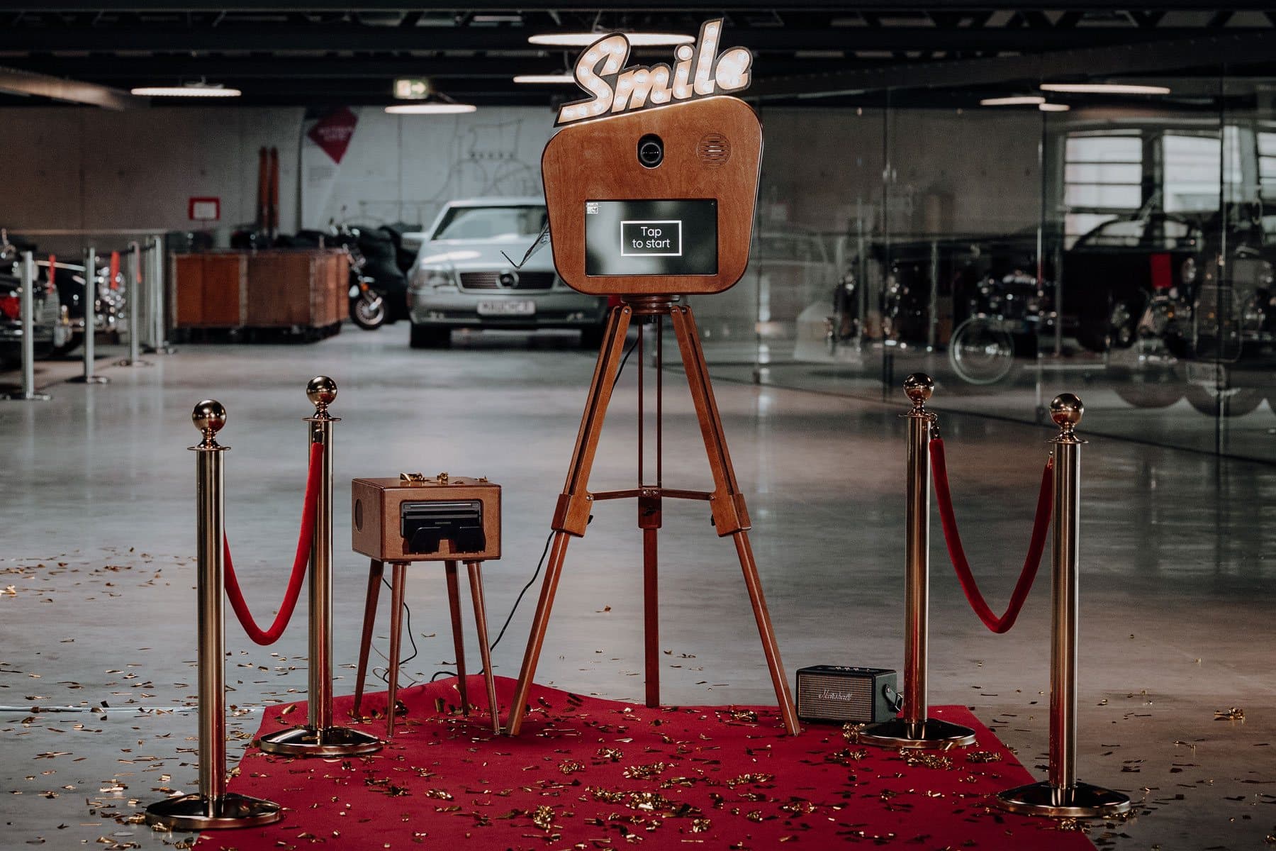 Fotobox «Smile» am Firmenevent auf rotem Teppich mit Absperrpfosten, Konfetti und Lautsprecher in einer Oldtimerhalle