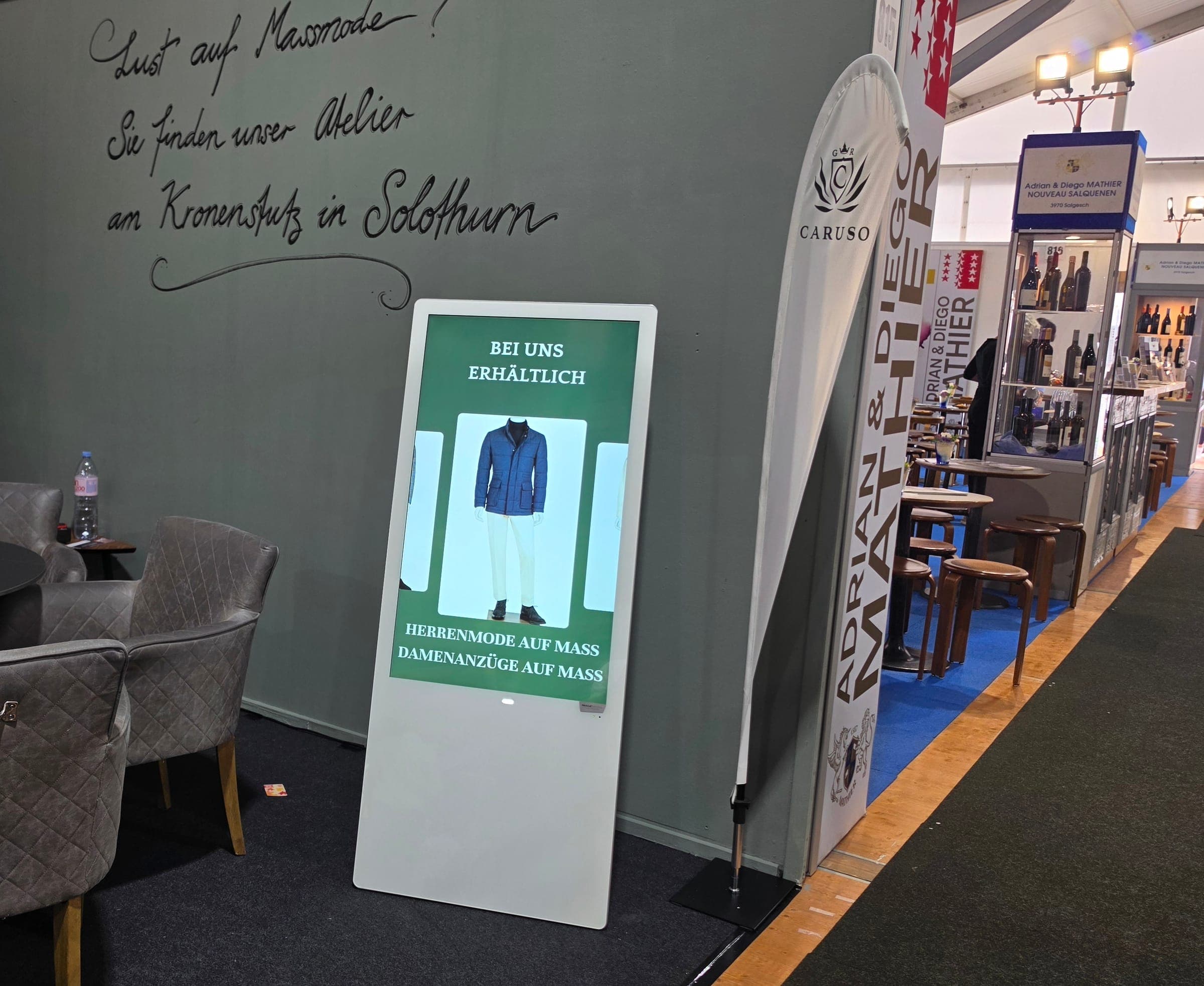 Digital-Signage-Screen im Hochformat am Messestand von Caruso Massmode an der HESO