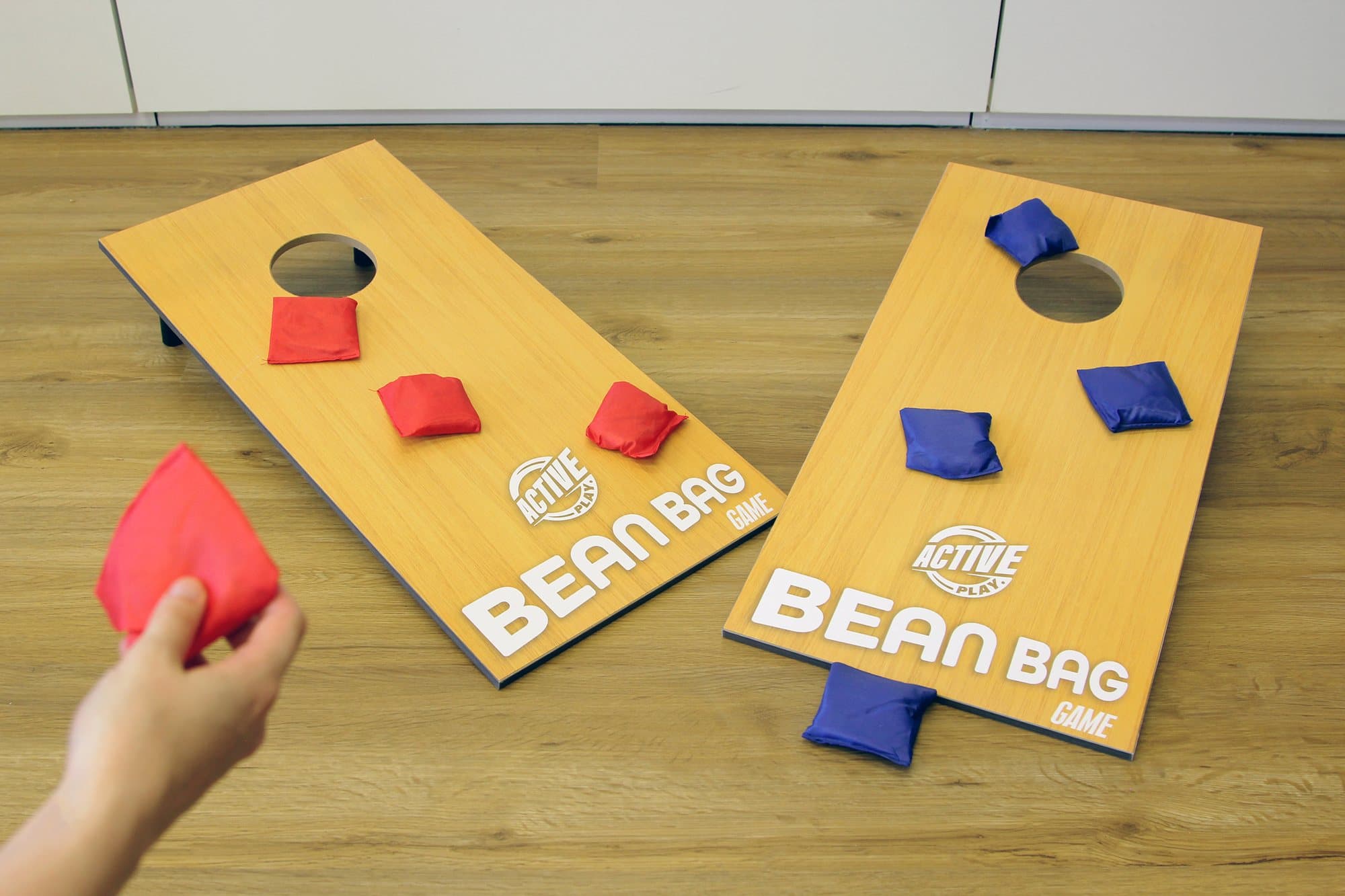 Cornhole mieten: zwei Holz-Wurfplatten mit roten und blauen Säckchen, eine Hand wirft