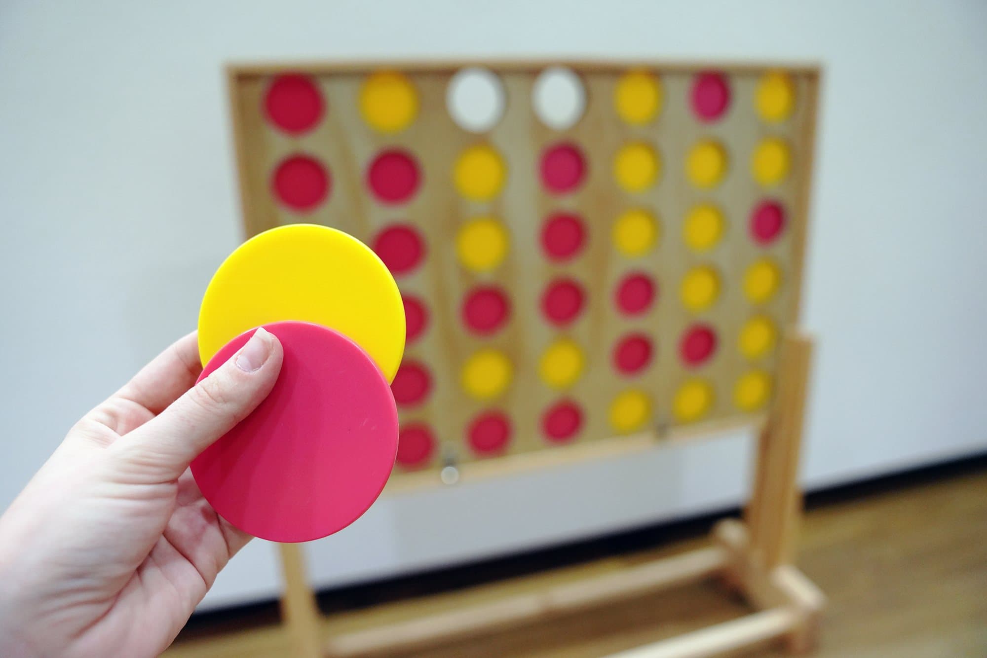 Vier gewinnt XXL mieten: Hand setzt gelbe und pinke Scheiben ins grosse Holzspielbrett